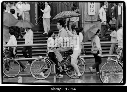 Chine Shanghai quelques jours après le massacre de la place Tiananmen en juin 1989. Les numérisations effectuées en 2018, hommes et femmes sur les bicyclettes à Shanghai sous la pluie. Banque D'Images