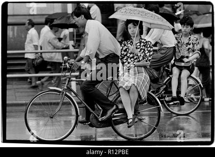 Chine Shanghai quelques jours après le massacre de la place Tiananmen en juin 1989. Les numérisations effectuées en 2018, hommes et femmes sur les bicyclettes à Shanghai sous la pluie. Banque D'Images