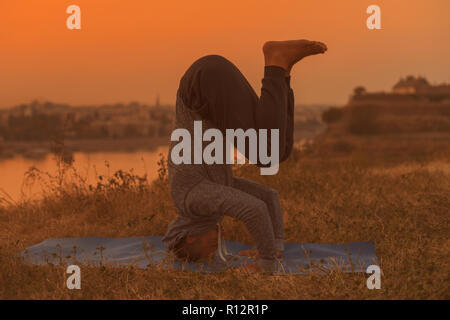 Man doing yoga sur le coucher du soleil avec vue sur la ville, Wavecrest /Shirshasana. Banque D'Images