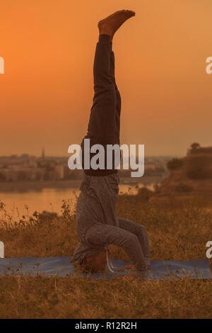 Man doing yoga sur le coucher du soleil avec vue sur la ville, Wavecrest /Shirshasana. Banque D'Images