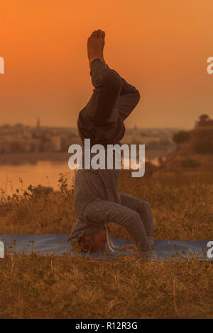 Man doing yoga sur le coucher du soleil avec vue sur la ville, Wavecrest /Shirshasana. Banque D'Images