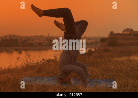 Man doing yoga sur le coucher du soleil avec vue sur la ville, Wavecrest /Shirshasana. Banque D'Images