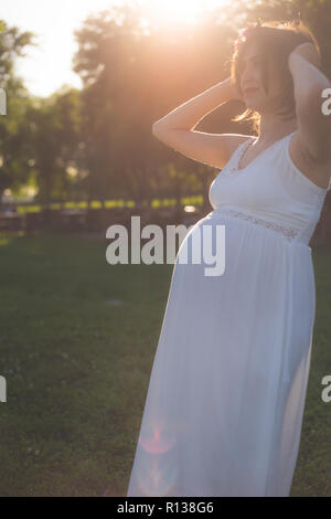 Belles femmes enceintes smiling au coucher du soleil Banque D'Images