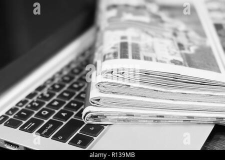 Journaux et ordinateur portable. Pile de quotidiens avec des news sur ordinateur. Avec Pages, des articles pliés et empilés sur le clavier de l'appareil électronique Banque D'Images