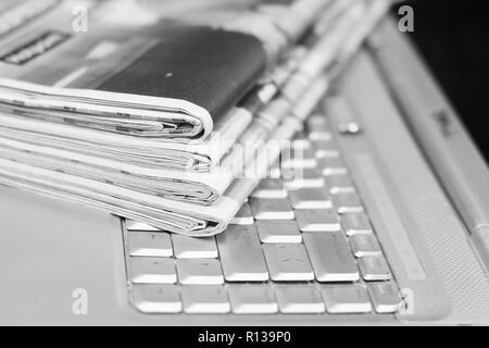 Journaux et ordinateur portable. Pile de quotidiens avec des news sur ordinateur. Avec Pages, des articles pliés et empilés sur le clavier de l'appareil électronique Banque D'Images