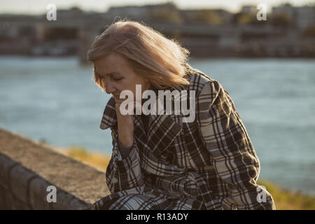 Sad senior woman sitting par la rivière seul. Banque D'Images