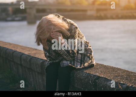 Sad senior woman sitting par la rivière seul. Banque D'Images