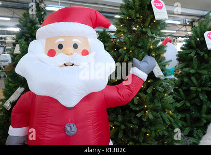 Père Noël gonflable en face d'arbres de Noël artificiels en vente en UK garden centre Banque D'Images