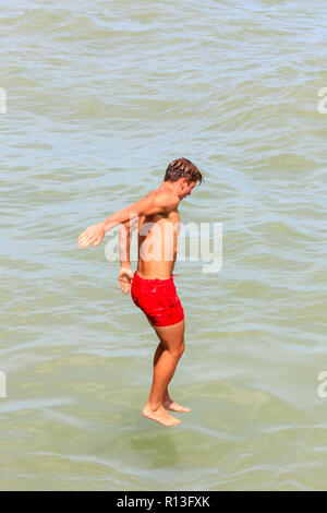 Jeune homme, adolescent, désactivation, sauter dans la mer au large de Broadstairs port. Les lignes rouges s'use, les pieds touchant à peine la mer. Banque D'Images