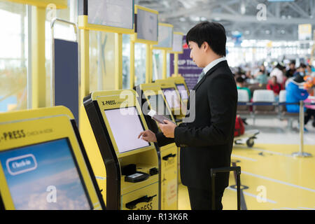 Les voyages d'affaires - Asian business man en utilisant l'enregistrement automatique dans les kiosques à l'aéroport. La technologie dans l'aéroport. Banque D'Images