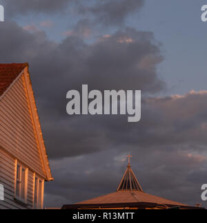 La lumière du soleil de fin de soirée s'allume sur le toit d'une maison et la croix d'une église contre les nuages de tempête sombre Banque D'Images