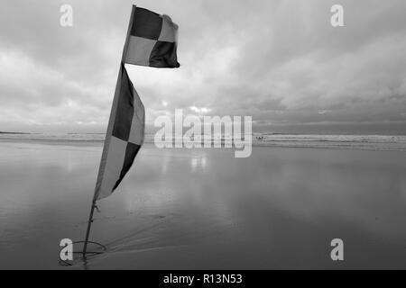 La plage de la baie de Croyde Devon du Nord à un coup de vent montrant lifeguard drapeaux en premier plan en noir et blanc Banque D'Images