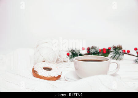 Une tasse de café et des décorations de Noël sous la forme d'un beignet sur un thread d'arrière-plan en bois blanc pour le tricot et un brin de sapin décoré avec Banque D'Images