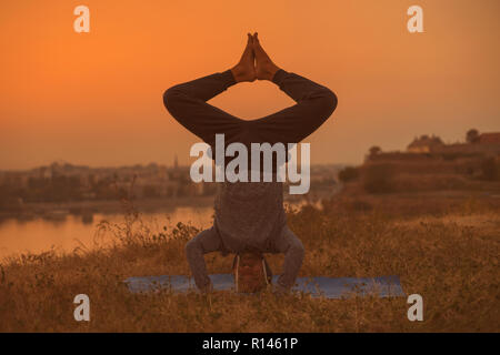 Man doing yoga sur le coucher du soleil avec vue sur la ville, Wavecrest /Shirshasana. Banque D'Images