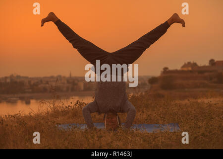 Man doing yoga sur le coucher du soleil avec vue sur la ville, Wavecrest /Shirshasana. Banque D'Images