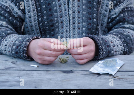 Close-up of a mans mains briser les bourgeons de marijuana à côté d'un dispensaire et un sac de joint. Banque D'Images