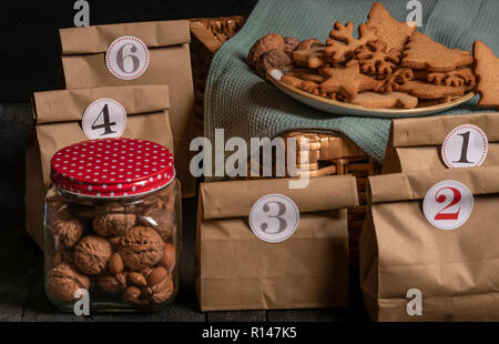 Concept de calendrier de l'avent avec les sacs en papier avec des nombres sur eux, un pot de noix et amandes et une plaque avec des biscuits au gingembre. Banque D'Images