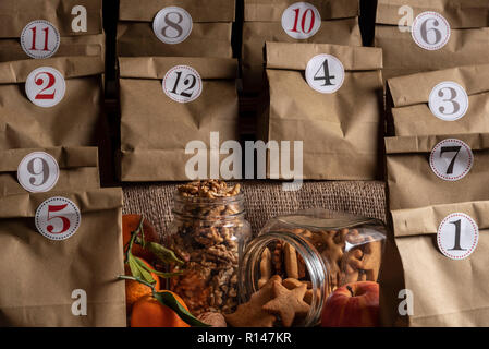 Calendrier de l'avent fait main avec beaucoup de sacs de papier brun classique avec des nombres sur eux et au milieu d'un pot avec des noix et un avec les cookies. Banque D'Images