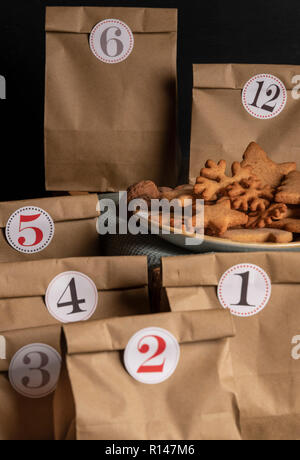 Les sacs en papier avec des nombres sur eux et une plaque avec des biscuits au gingembre. Calendrier de l'avent fait main. Banque D'Images