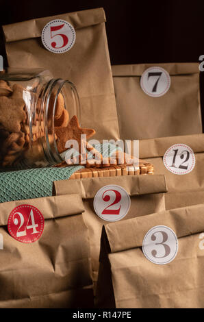 Pot en verre renversée, pleine de gingerbread cookies de Noël entouré par les sacs en papier avec des nombres sur eux. Calendrier de l'Avent. Banque D'Images