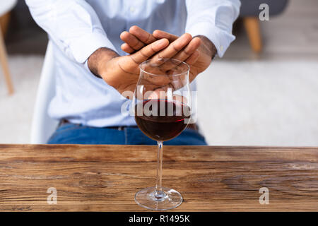 La main de l'homme faire aucun geste pour verre de vin sur un bureau en bois Banque D'Images