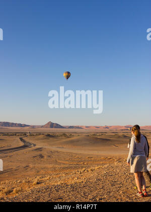 Tourist couple stand et regarder la montgolfière dans le ciel bleu à l'entrée du Parc National Namib Naukluft Sossusvlei en Namibie Banque D'Images