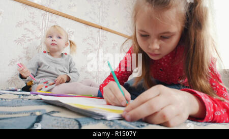 Cute petite fille s'appuyant sur un livre de coloriage tout en se trouvant sur le plancher Banque D'Images