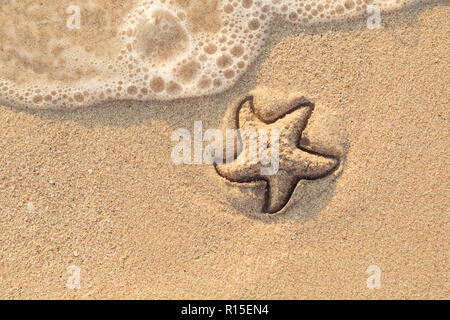 Étoile de dessiné sur la plage sable être emportée par une vague. Le moussage mer vague venant de laver une photo sur du sable de plage jaune humide. Maison de vacances et vocation Banque D'Images