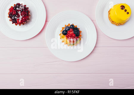 Composition de trois délicieux desserts tartelettes sur table en bois rose, vue du dessus. Mise à plat de l'arrangement des friandises avec copie espace. Banque D'Images