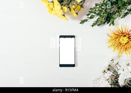 Vue de dessus de la maquette téléphone mobile avec écran blanc parmi les laïcs de châssis plat fleurs et branches vertes, copiez l'espace. Banque D'Images