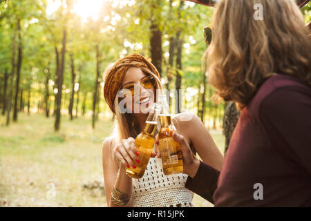Photo de l'heureux couple hipsters homme et femme rire et boire de la bière en forêt Banque D'Images
