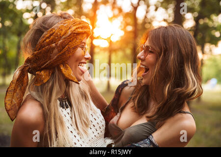 Photo de deux belles femmes hippie souriant et serrant les uns les autres en marchant dans la forêt Banque D'Images