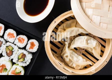 Gyoza ou raviolis vapeur traditionnel servi en sushi et sur fond noir. Mise à plat de la composition du haut vers le bas Banque D'Images