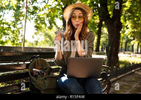 Photo de belle jeune femme heureux excité à l'extérieur assis using laptop computer holding credit card. Banque D'Images