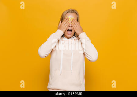 Photo de peur jeune femme avec appareil dentaire couvrant les yeux sur fond jaune isolé Banque D'Images