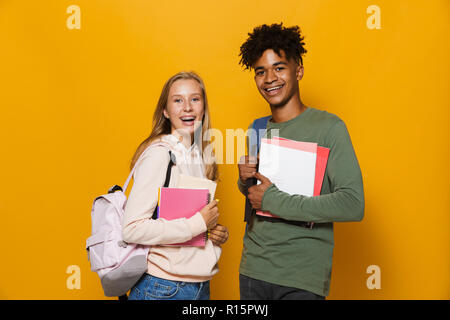 Photo de happy students guy and girl 16-18 portant des sacs à dos de sourire et de tenir les livres d'exercice isolé sur fond jaune Banque D'Images