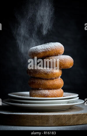 Pile de 5 donuts sucre sucré sur petite pile de 3 plaques blanches sur planche de bois avec fond gris foncé être dépoussiéré et recouvert de sucre glace. Copie Banque D'Images