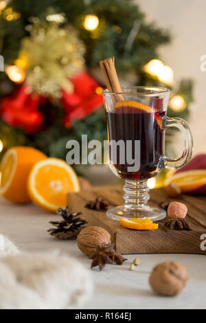 Composition d'hiver. Vin chaud en verre sur bois à fond blanc. Couronne de sapin, des cloches, des guirlandes et de guirlandes, nappes, orange, cannelle et d'épices Banque D'Images