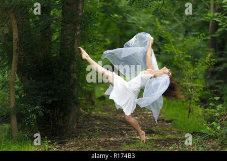 Portrait mystique d'une belle femme nu gracieux dans une robe blanche avec ses bras drapé de tissu transparent vaporeuses qui posent avec une jambe soulevée Banque D'Images