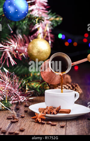 Café aromatisé est versé depuis le café turc dans une tasse de café. La cannelle et badiane sur une table en bois. Concept de Noël. Banque D'Images