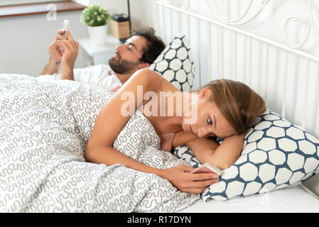 Jeune couple avec les smartphones dans leur lit. Mauvaise relation concept Banque D'Images