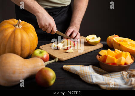 Les cuire l'apple en morceaux pour la cuisson. Sur un tableau noir en bois se trouvent les potirons de tailles et de formes diverses, pommes mûres, un bol et un torchon Banque D'Images