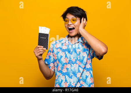 Portrait d'un homme asiatique joyeuse sur fond jaune isolé, holding passport avec billets de vol Banque D'Images