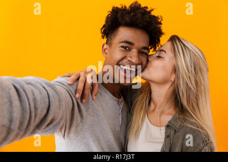 Image jeune couple aimant posant sur fond jaune isolé hugging prendre une caméra en s'embrassant. selfies Banque D'Images