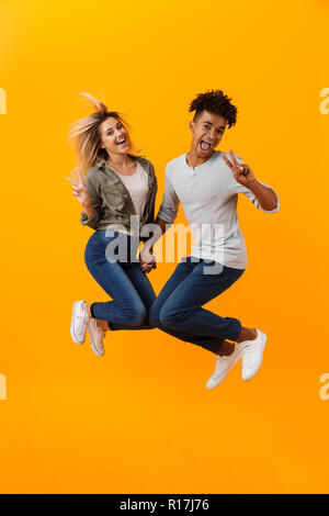 Photo de happy young couple aimant isolé sur fond jaune saut montrant la paix geste. Banque D'Images