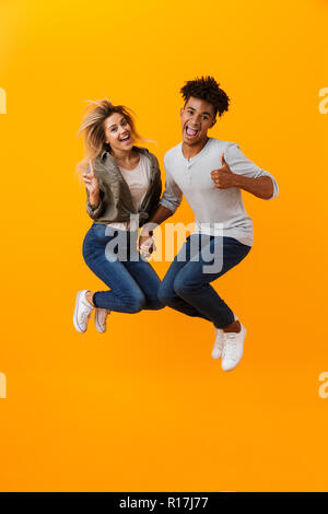 Photo de happy young couple aimant isolé sur fond jaune saut showing Thumbs up. Banque D'Images