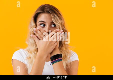 Photo de femme blonde surpris en vêtements de base couvrant la bouche avec les mains sur fond jaune isolé Banque D'Images