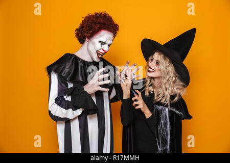 Image de sorcière femme et joker homme portant costume noir et maquillage halloween jouer autour sur fond jaune isolé Banque D'Images