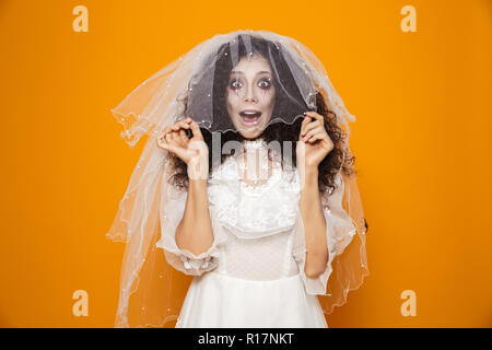 Photo de femme horrible sur halloween portant robe de mariage et de vacances toucher maquillage voile blanc sur fond jaune isolé Banque D'Images