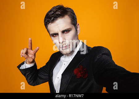 Photo de zombie effrayant halloween sur l'homme portant costume classique et creepy en tenant un miroir sur fond jaune isolé selfies Banque D'Images